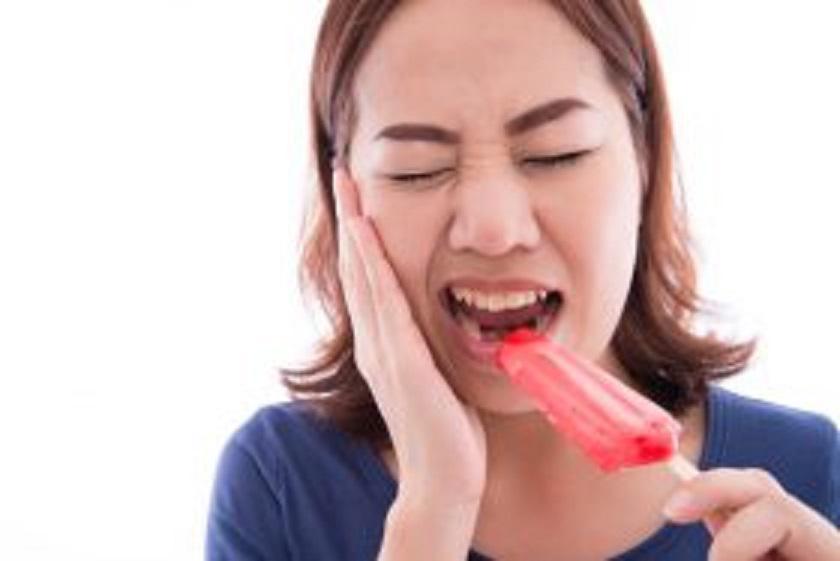 Woman with tooth sensitivity biting down on cold popsicle