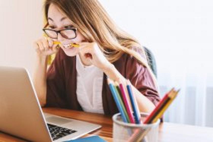 Woman at computer biting down on a pencil