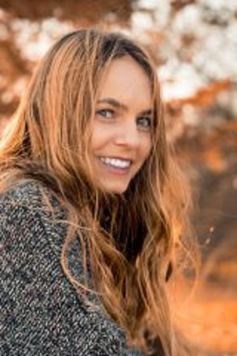 Woman in warm clothing standing in front of fall foliage smiling