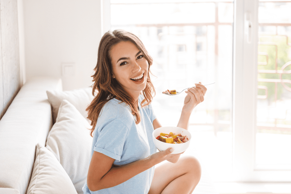 Woman smiling while eating cereal in a brightly lit room