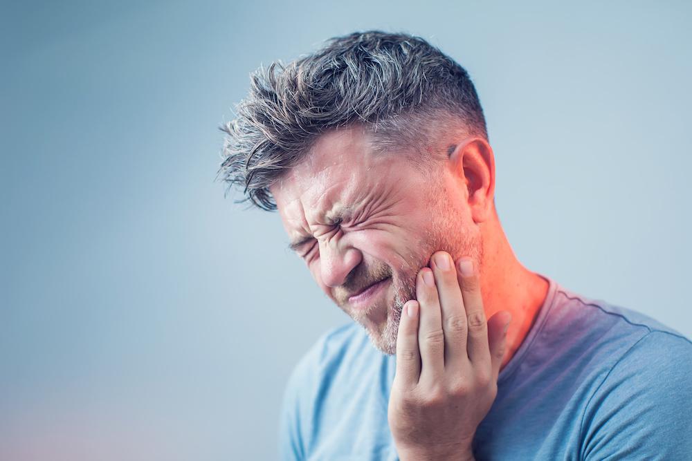 Man holding jaw in pain while wincing