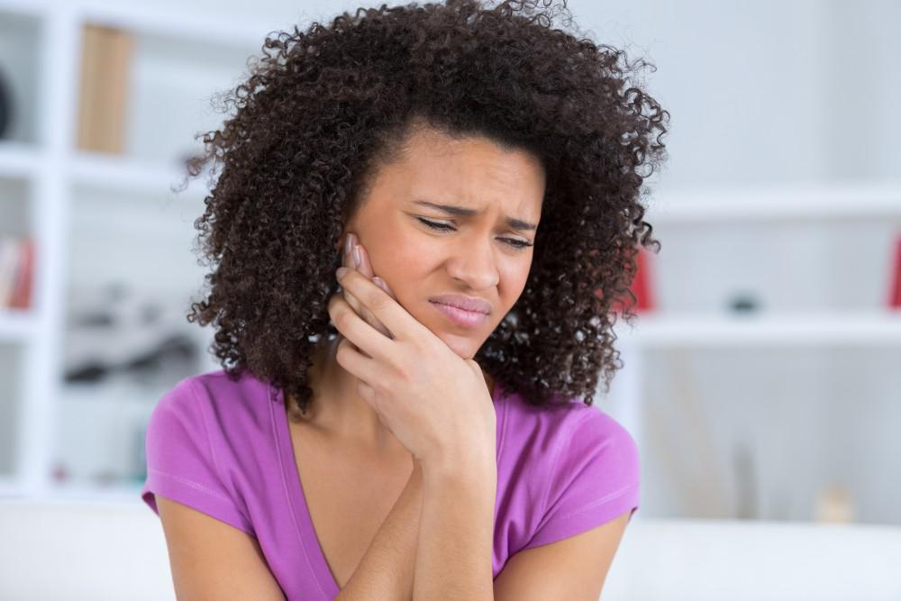 Woman holding her hand up to her jaw while wincing in pain