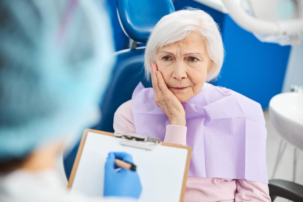 Elderly lady holding a hand up to her jaw in pain while at dentist