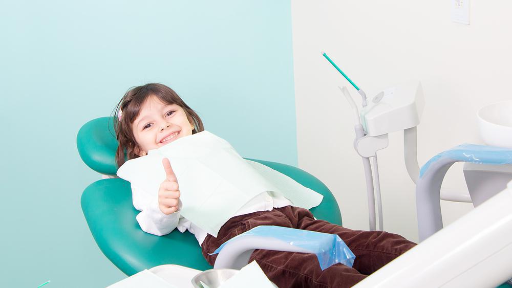 Smiling child in dental office doing a thumbs up gesture.
